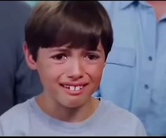 a young boy smiles while standing in front of an older man wearing a blue shirt