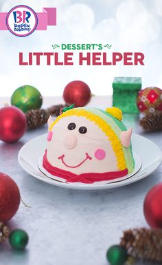 a little helper cake sitting on top of a white plate next to christmas ornaments