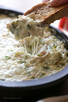 a person is dipping some bread into a bowl of broccoli and cheese dip