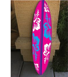 a pink and blue surfboard sitting on top of a cement wall next to a plant