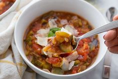 a white bowl filled with vegetable soup on top of a table next to a napkin