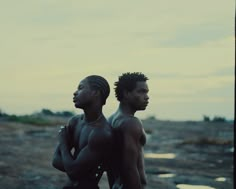 two black men standing next to each other on a rocky beach with the sky in the background