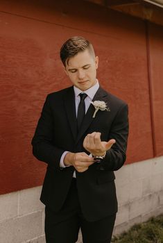 a man in a black suit and white flower boutonniere standing next to a red wall