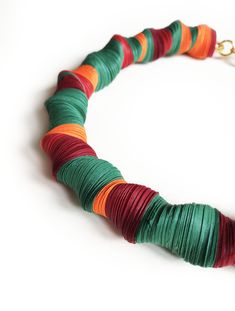 a necklace made out of multicolored paper on a white surface with a gold chain