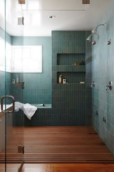 a green tiled bathroom with wood flooring and glass shower door, built in shelves on the wall