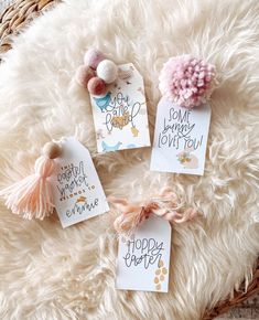 three small tags with pom poms on them sitting on a fluffy white blanket