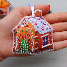 a hand holding an ornament shaped like a gingerbread house