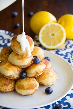 a stack of pancakes with blueberries and lemons on the side, being drizzled with icing