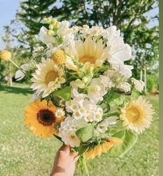 a person holding a bouquet of sunflowers and daisies in their hand on the grass