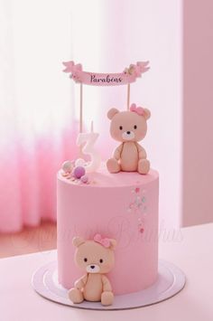 a pink cake with two teddy bears on top and a name sign above the bear