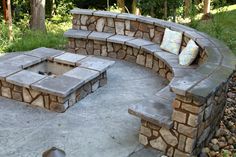 an outdoor fire pit surrounded by stone walls and seating area with pillows on the cushions