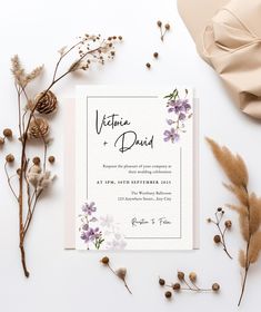 a wedding card with purple flowers and greenery on the side, next to some dried plants