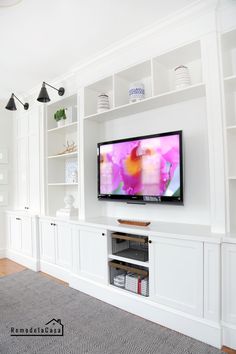 a flat screen tv sitting on top of a white bookcase in a living room