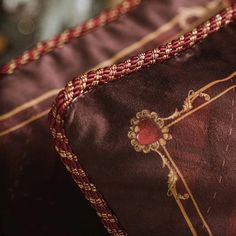 a close up of a decorative pillow on a bed with red and gold trimmings