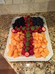 a white platter filled with cut up fruit on top of a marble countertop