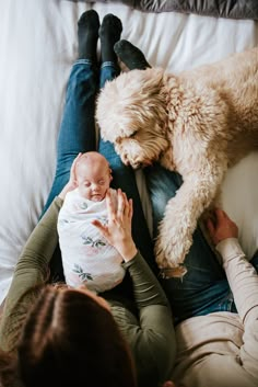 a woman holding a baby while laying next to a dog