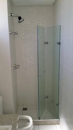 a bathroom with a glass shower door and white tile flooring on the walls, along with a sink and toilet