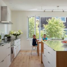 two children sitting at a table in a large kitchen with white cabinets and wood floors