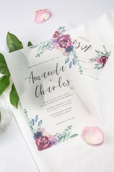 wedding stationery with flowers and greenery on white paper next to pink rose petals