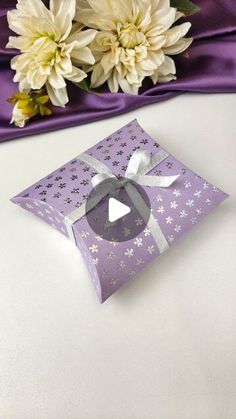 a purple gift box with white flowers in the background and a purple satin table cloth