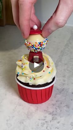 a cupcake being dunked with icing and sprinkles by someone's hand