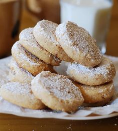 a pile of sugar cookies sitting on top of a white plate next to a glass of milk