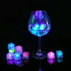 a wine glass filled with glowing cubes on top of a black table next to it