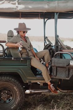 a woman sitting on the back of a green jeep with a bottle in her hand