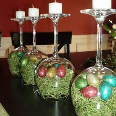 three wine glasses filled with easter eggs on top of a wooden table next to candles