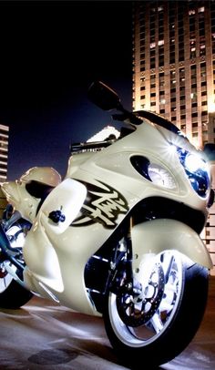 a white motorcycle is parked in front of some tall buildings at night with its lights on