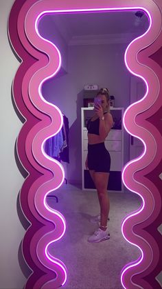 a woman taking a selfie in front of a mirror with pink and purple wavy shapes