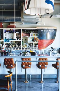 a bar with leather chairs and shelves filled with bottles on the wall behind it,