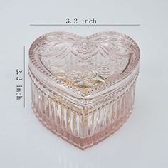 a pink heart shaped glass box sitting on top of a white table next to a ruler