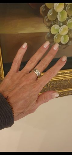 a woman's hand with a ring on it next to a painting and grapes