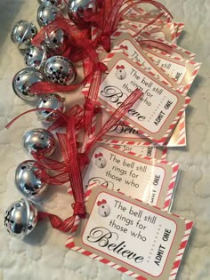 some silver bells and red ribbon on top of a white table with two tags that say believe, the bell still has three holes for those who