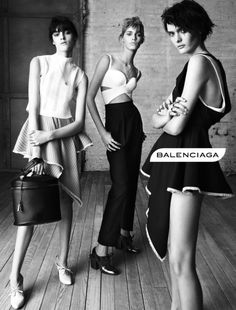 three young women standing next to each other on a wooden floor in front of a brick wall