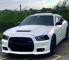 a white dodge charger parked in a parking lot next to a fence and grass