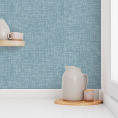 two white vases are sitting on a shelf in front of a gray wallpaper