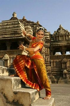 a woman in an orange and yellow sari is sitting on some steps near a building