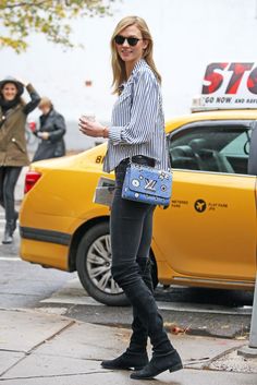 a woman is standing on the sidewalk with her hand in her pocket and holding a blue purse