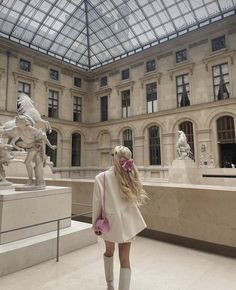 a woman standing in front of a building with a horse statue on the other side