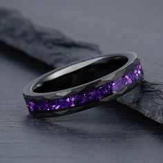 two wedding bands with purple stones in them sitting on a piece of wood next to a rock