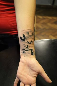 a person with a tattoo on their wrist holding up her hand to the sky and flying bats