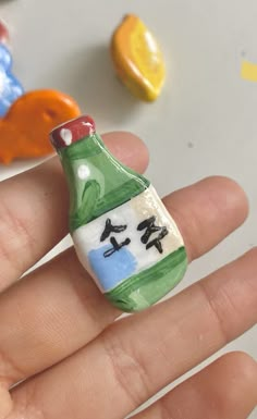 a hand holding a miniature bottle with writing on it and other small objects in the background