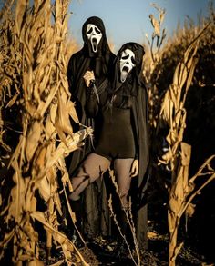 two people dressed in black and white are standing in a corn field with their faces painted