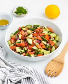 a white bowl filled with cucumber and tomato salad next to a wooden spoon