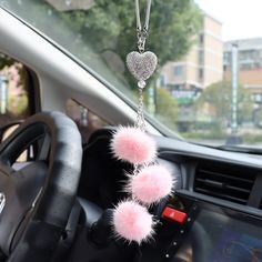 two pink pom - poms hanging from a car steering wheel chain on a dashboard