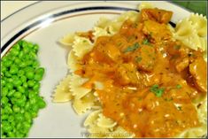 a white plate topped with pasta and meat covered in sauce next to green pea sprouts