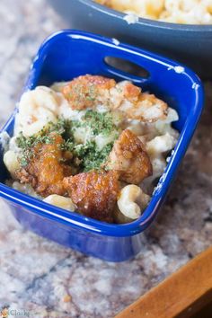 two blue containers filled with food on top of a counter next to another bowl full of macaroni and cheese