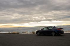 a car is parked on the side of the road near some hills and clouds in the sky